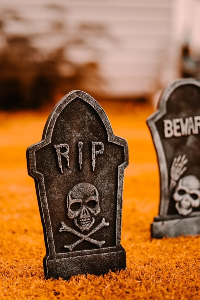 Decorative gravestones with inscription placed in yard on ground with dry grass near white building on blurred background during holiday celebration